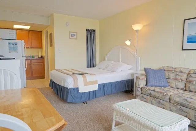 A studio with a queen bed, a patterned sofa bed and a wicker coffee table, with the kitchenette behind